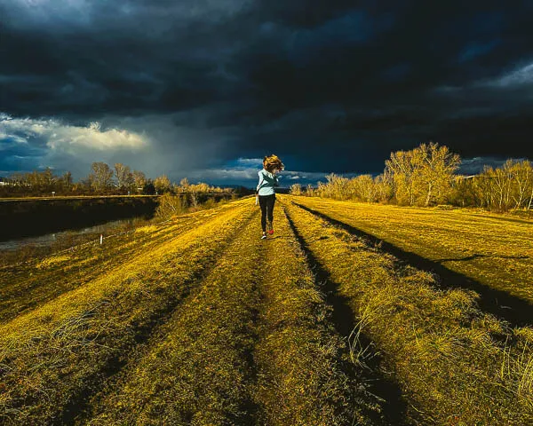 a woman running  down a dirt road under a cloudy sky